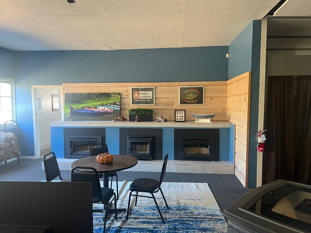 Village Hearth showroom lounge — three wood-burning inserts under Fireplace Xtrordinair and Lopi signage, with a table and chairs for customers